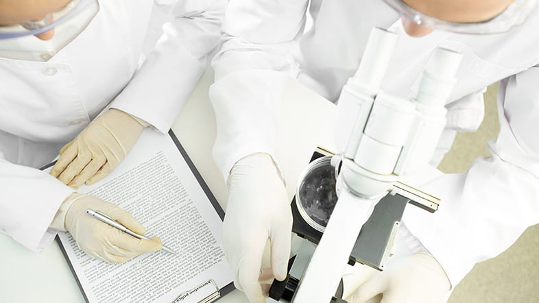 two scientists with microscopes taking notes