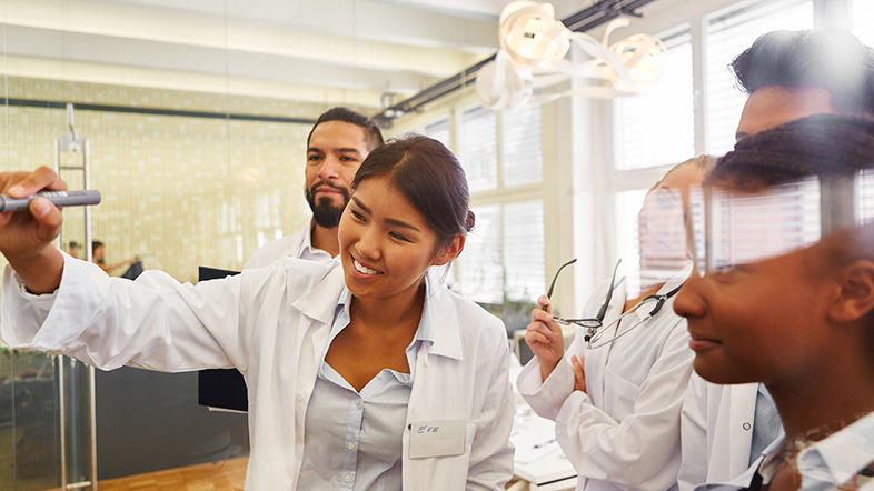 young female scientist in a group of young scientists taking notes on a flipboard