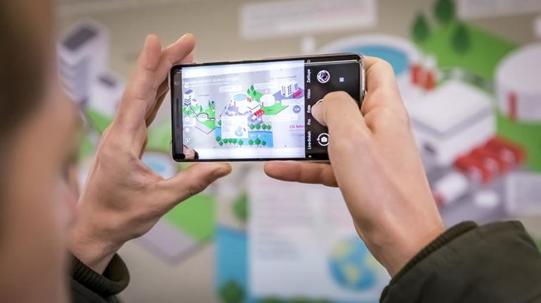 Homme photographiant sur son téléphone portable une affiche sur le projet d'assainissement du CSL Behring Bern.