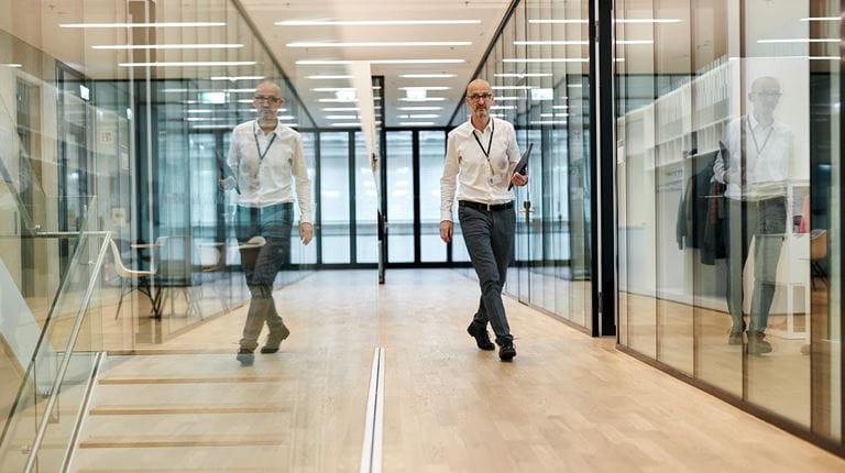 Research Manager Adrian Zuercher walks through sitem-insel his image reflected in glass walls